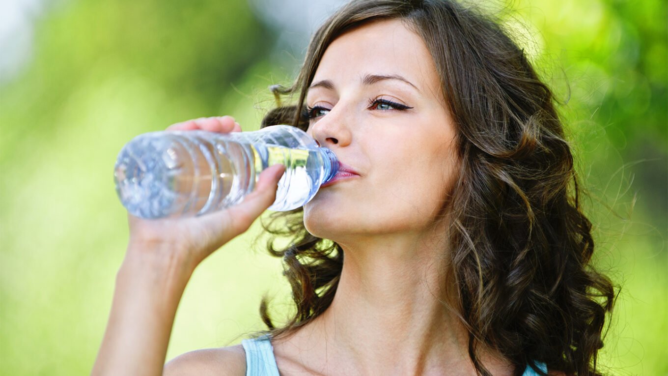 Woman drinking water and smiling – stay hydrated for better health.